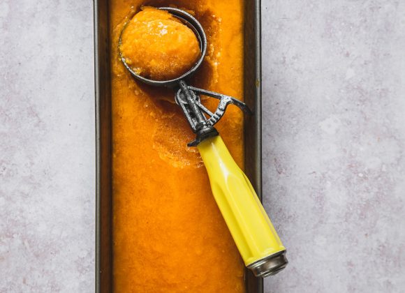 mango sorbet in an ice cream tin with an ice cream scoop