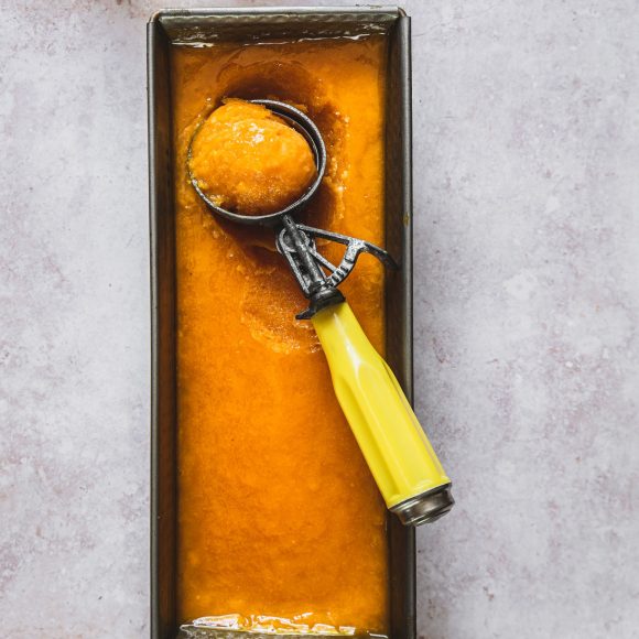 mango sorbet in an ice cream tin with an ice cream scoop